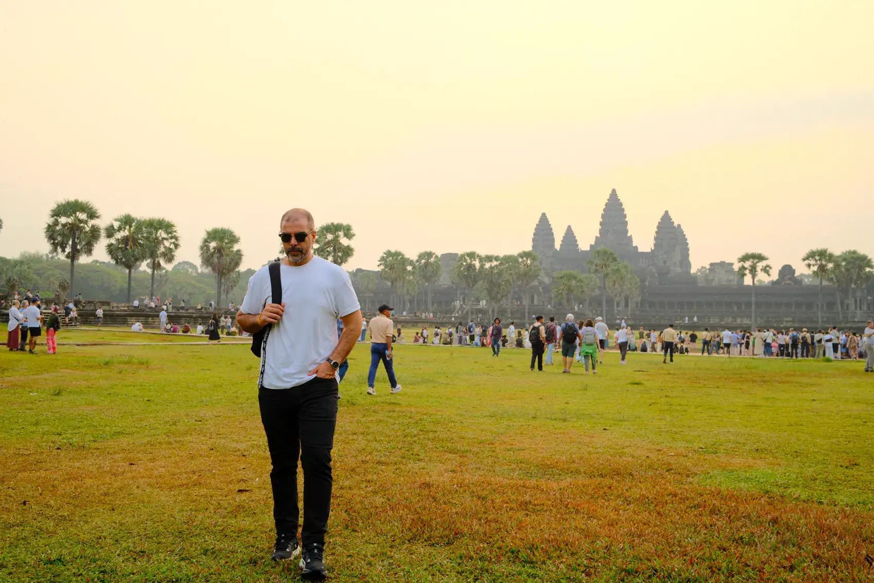 Un viajero caminando por el pasto al amanecer, con las torres de Angkor Wat de fondo