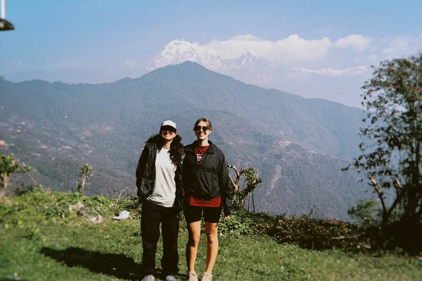 Dos viajeros parados en una ladera verde, con la montaña nevada de fondo